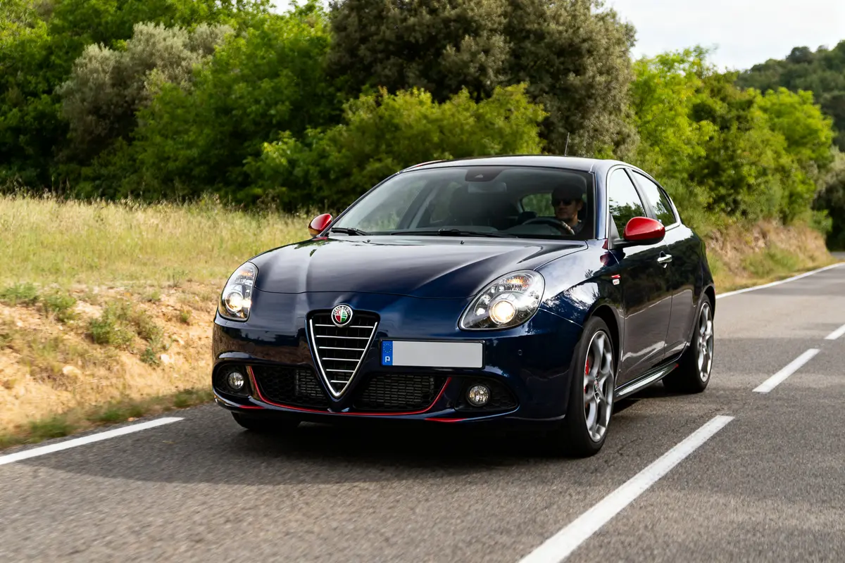 Voiture Alfa Romeo Giulietta Quadrifoglio roulant sur route bordée de verdure.