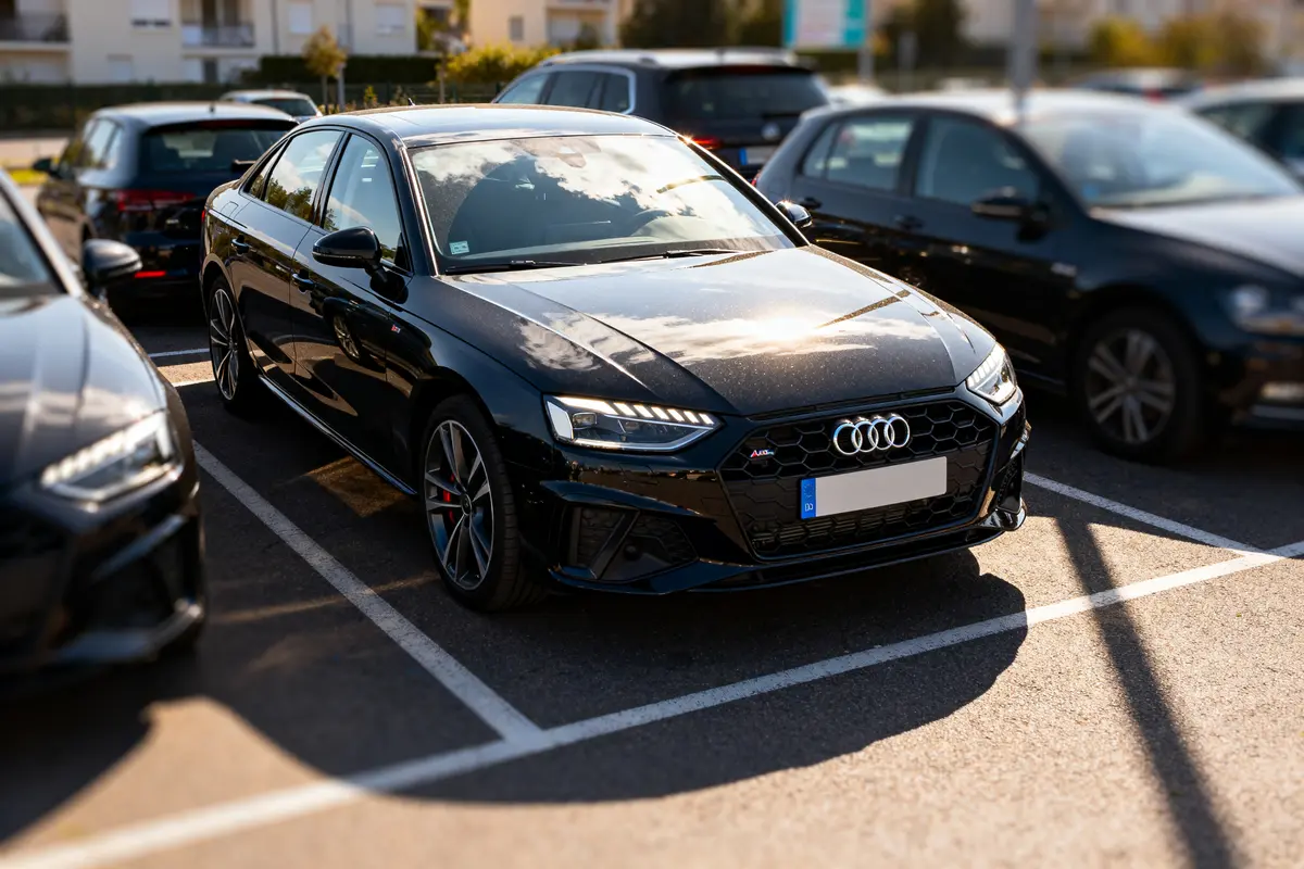 Audi A4 B9 noire stationnée sur un parking ensoleillé entre plusieurs voitures