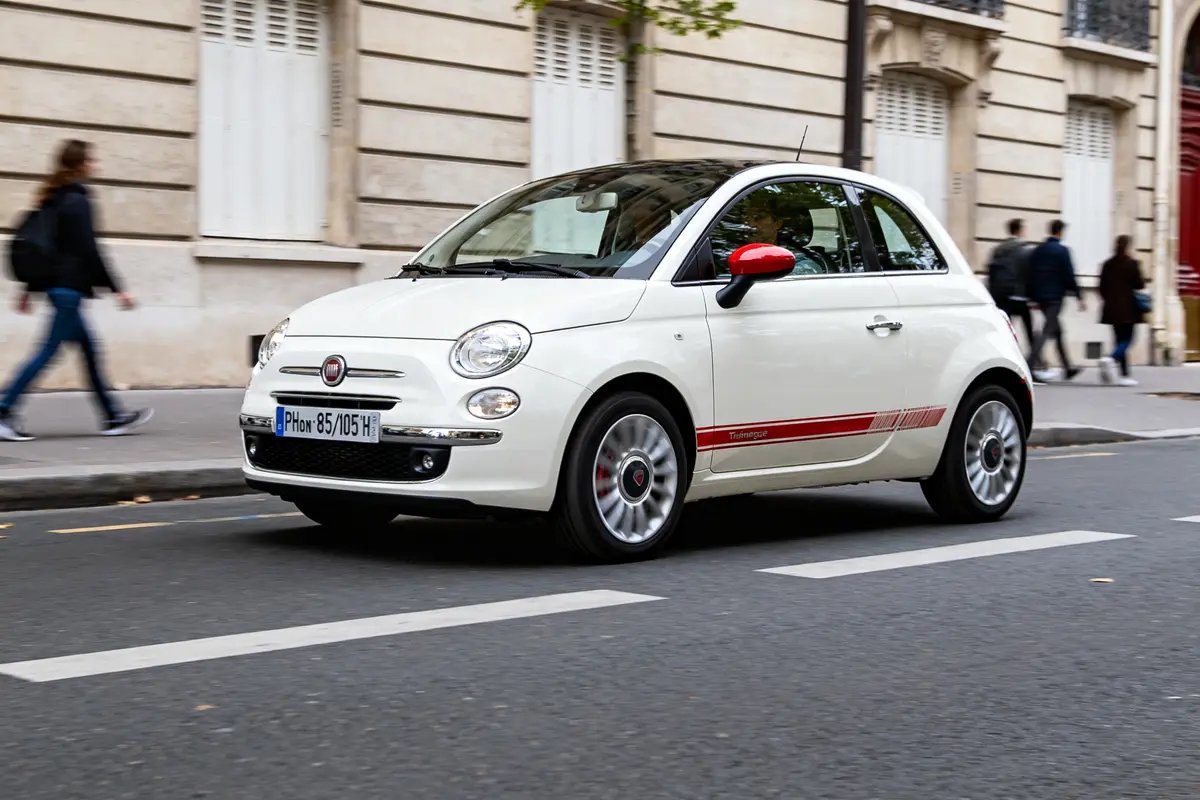 Fiat 500 Lounge blanche roule en ville avec rétroviseurs rouges et bande décorative
