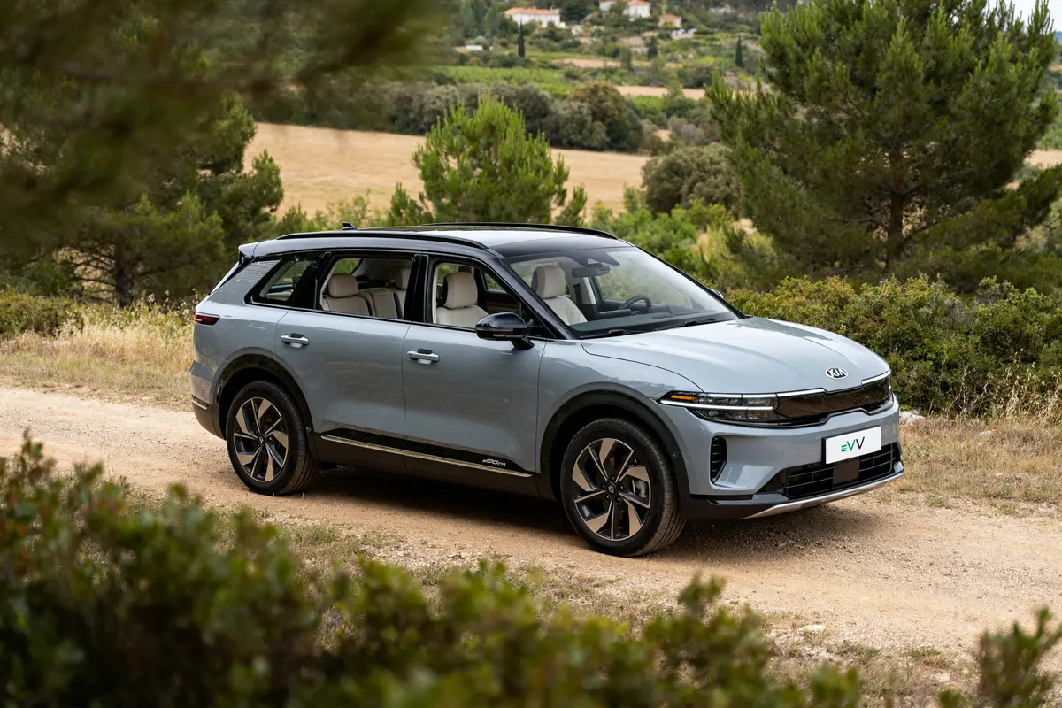 SUV électrique Kia EV7 bleu garé sur chemin de campagne entouré de verdure.