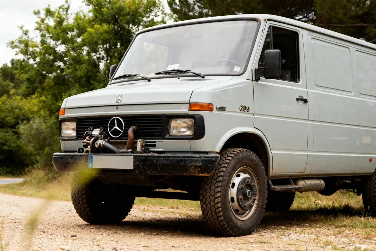 Mercedes 609 blanc garé sur chemin de terre entouré de végétation luxuriante