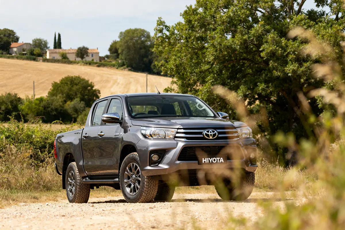 Toyota Hilux pick-up gris sur chemin rural avec paysage champêtre en arrière-plan