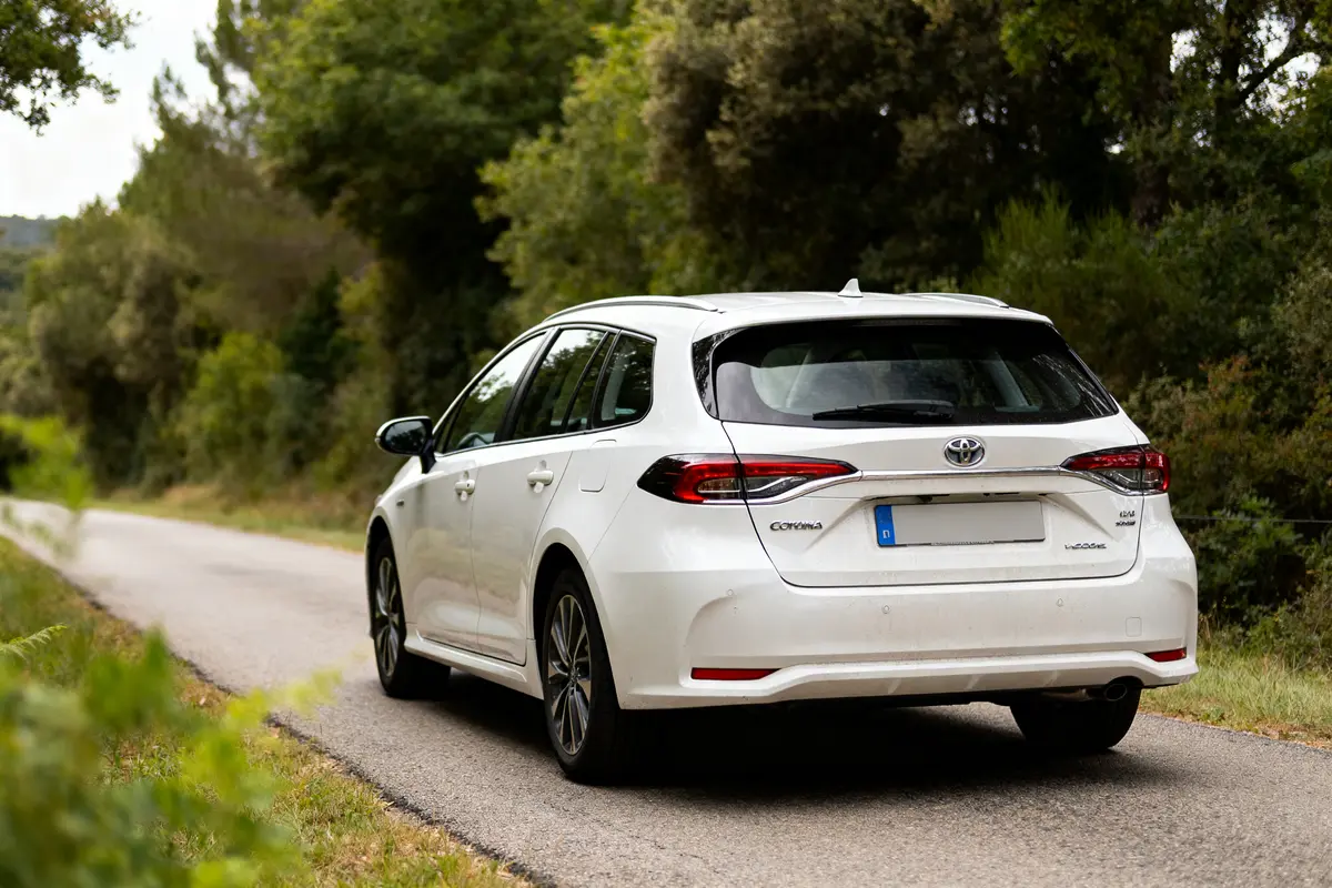 Voiture blanche Toyota Corolla Touring Sports sur route bordée d'arbres verdoyants