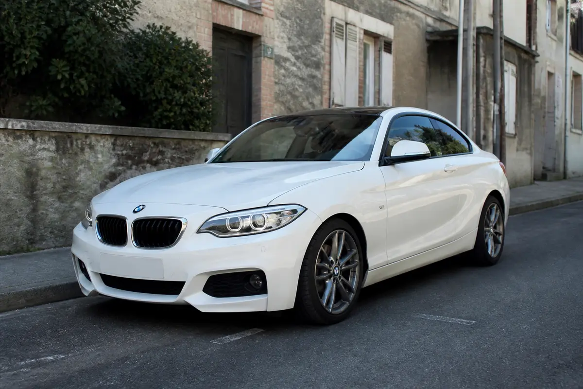 Voiture blanche BMW Série 220 stationnée dans une rue résidentielle ancienne.