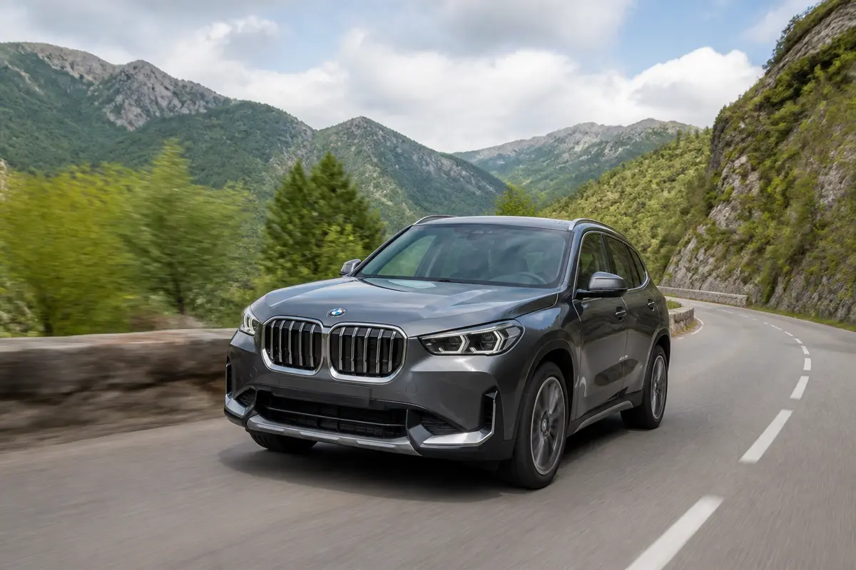 SUV BMW X1 gris parcourant une route de montagne avec verdure et ciel nuageux