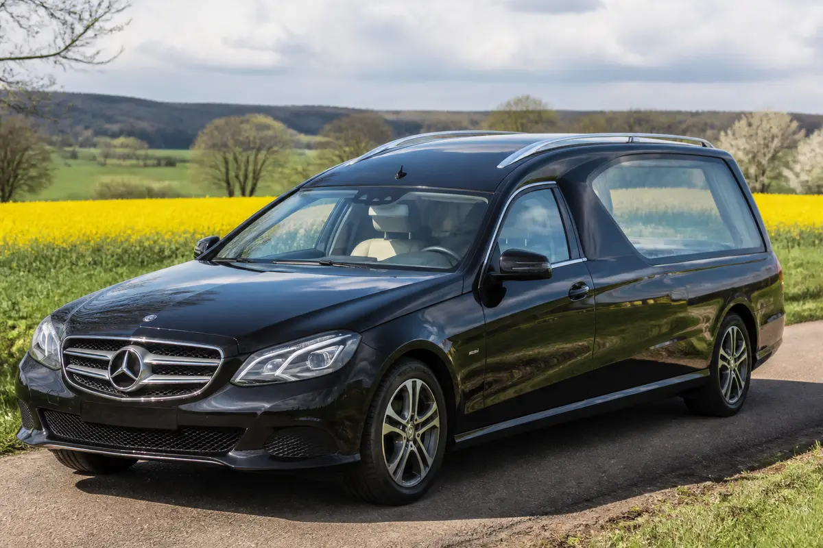 Corbillard Mercedes noir stationné sur une route de campagne verdoyante et fleurie